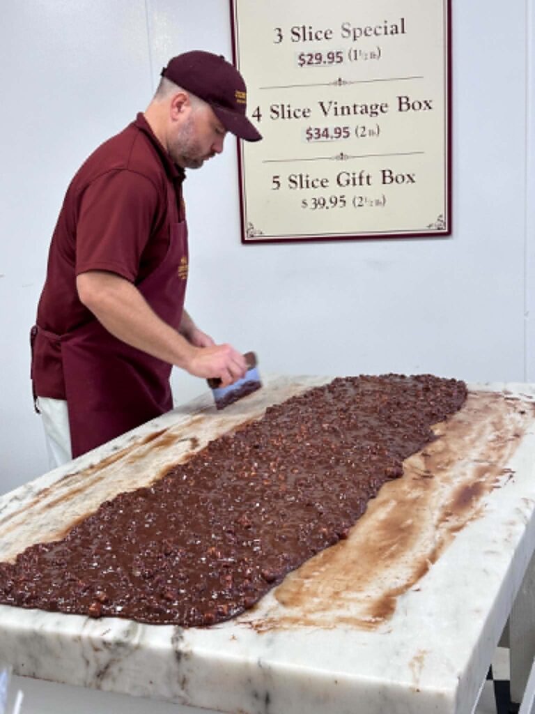 A fudge maker working a long slab of chocolate fudge on a marble table at a Mackinac Island fudge shop