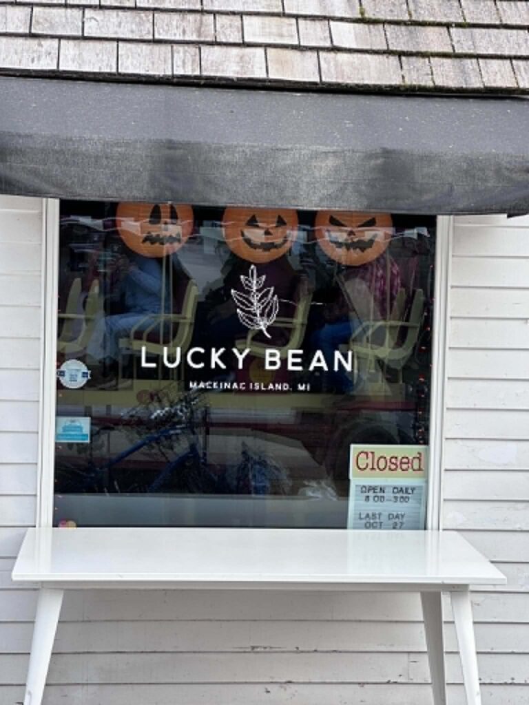 A Lucky Bean coffee shop window on Mackinac Island showing a Last Day Oct 27 seasonal closing sign