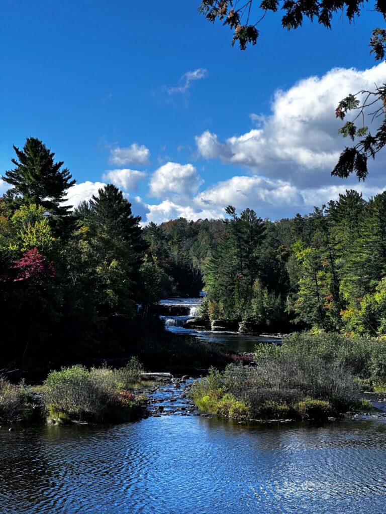 The Tahquamenon River near the Lower Falls on a perfect summer day with blue sky, white clouds, and lush green forest reflected in the calm water