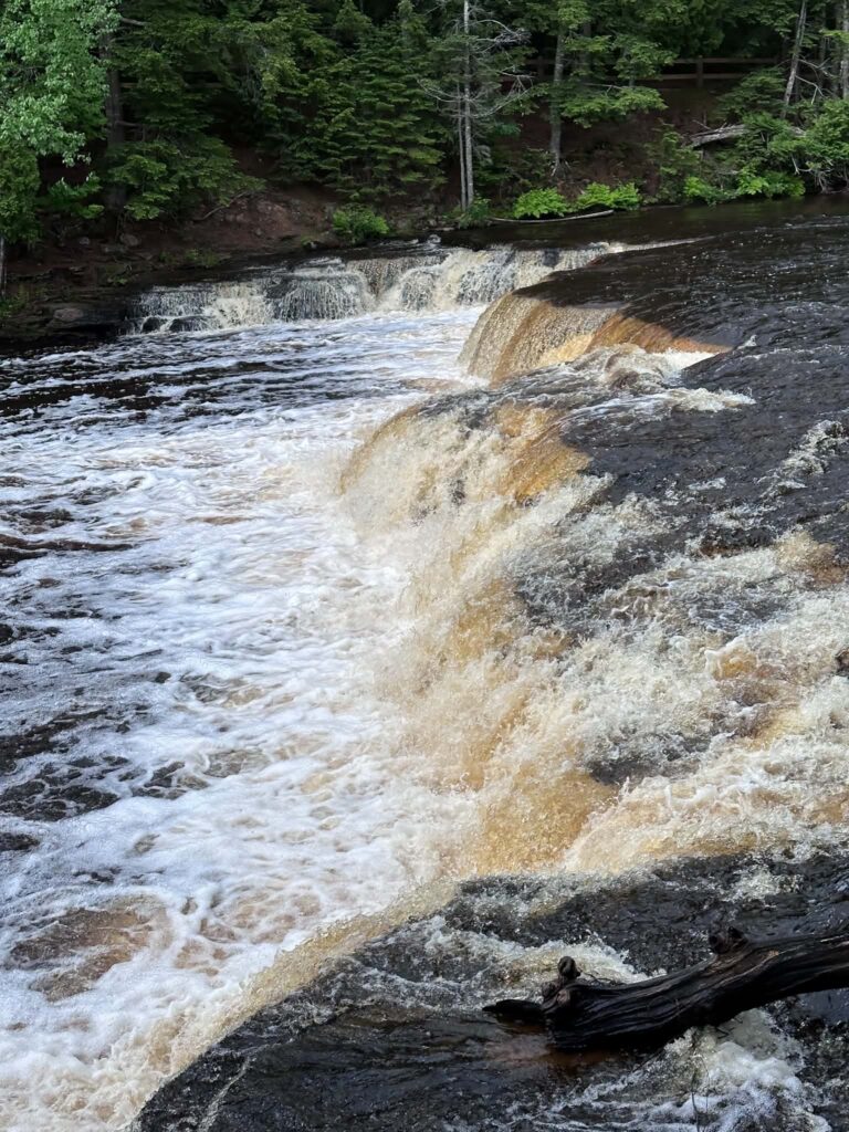 Close-up of churning brown amber water rushing over a Lower Tahquamenon Falls cascade with white foam