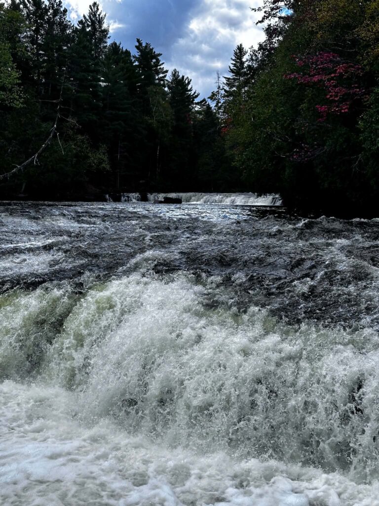A Lower Tahquamenon Falls cascade rushing through a narrow dark rocky channel in dramatic moody overcast light