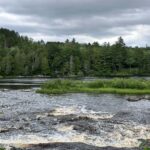 Lower Tahquamenon Falls under a dramatic overcast sky with dark clouds reflecting in the rushing amber water
