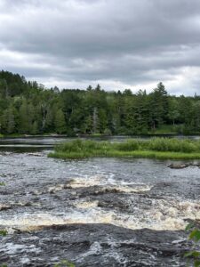 Lower Tahquamenon Falls under a dramatic overcast sky with dark clouds reflecting in the rushing amber water