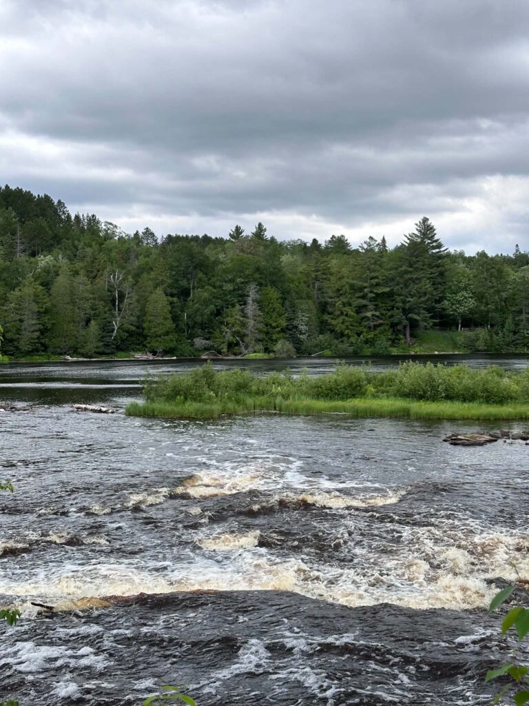 Lower Tahquamenon Falls under a dramatic overcast sky with dark clouds reflecting in the rushing amber water