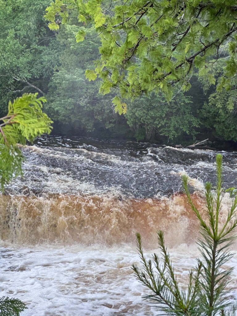 Elevated view of a Lower Tahquamenon Falls cascade with rocky shoreline and amber river water