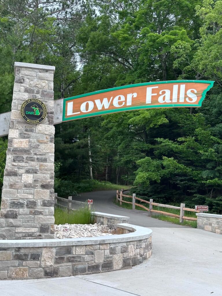 Stone entrance sign reading Lower Falls at Tahquamenon Falls State Park surrounded by green trees