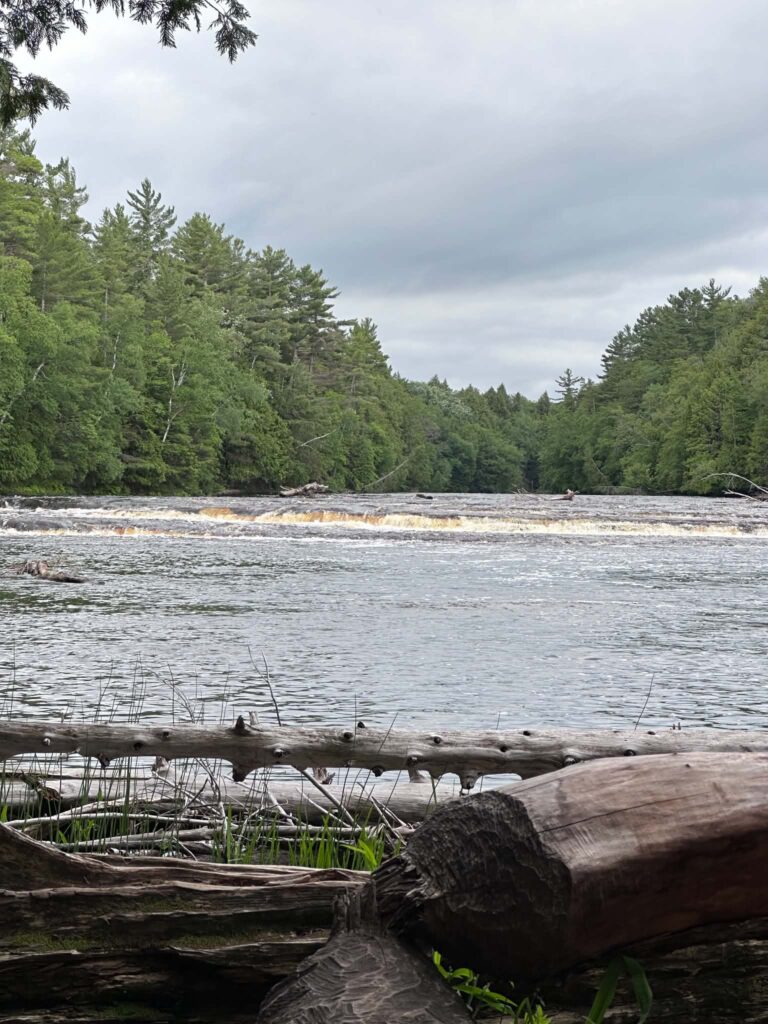 Wide exposed sandstone rock shelf along the Tahquamenon River at the Lower Falls with amber water flowing around i