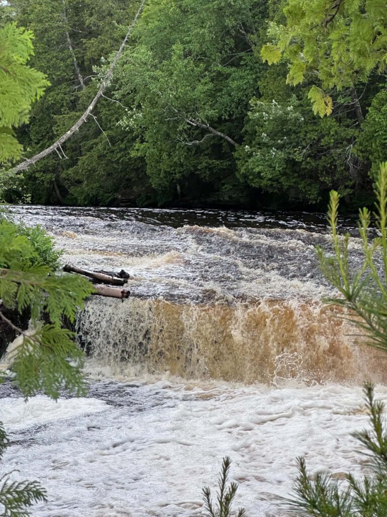Distant view of Lower Tahquamenon Falls from the river with a small watercraft visible on the amber water