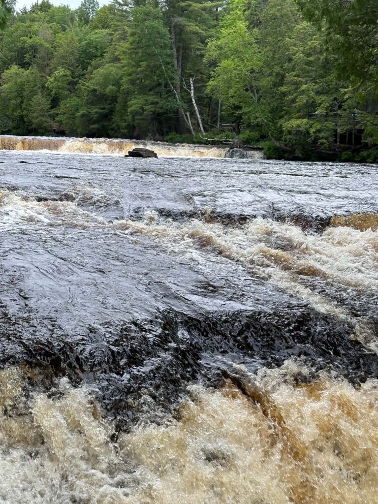 Lower Tahquamenon Falls at lower water level, with amber water cascading over dark wet rocks in a moody overcast light