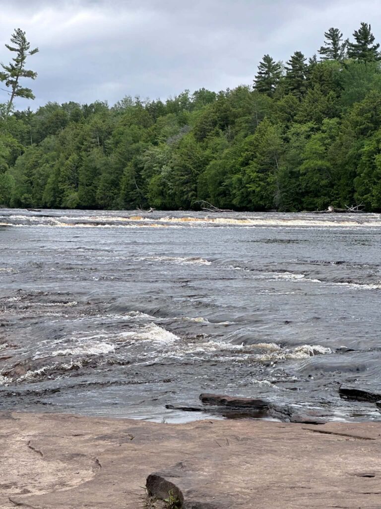 Wide view of amber-colored water cascading over multiple rock tiers at the Lower Tahquamenon Falls