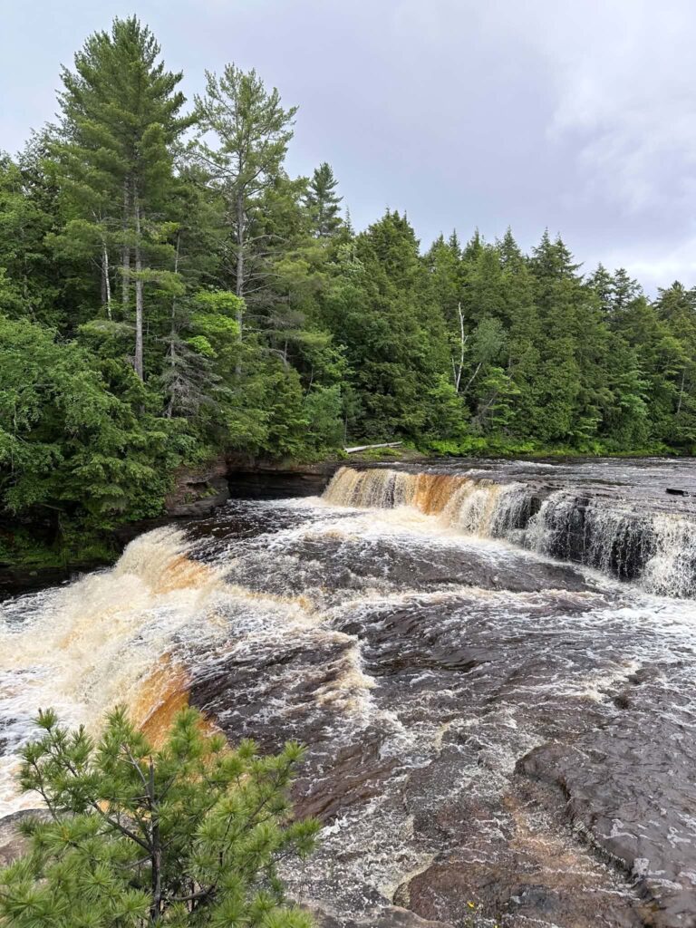 Summer view of a Lower Tahquamenon Falls cascade surrounded by lush green forest on both banks of the river