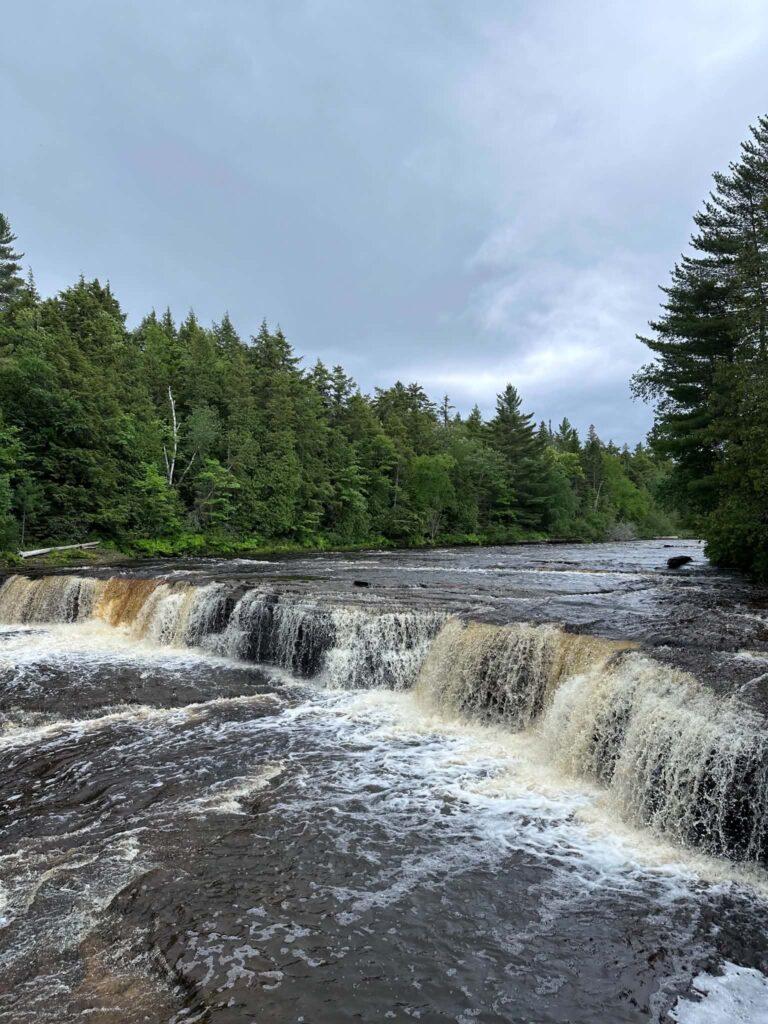 The Tahquamenon River splitting around a rocky island at the Lower Falls, showing two separate cascades flowing side by side
