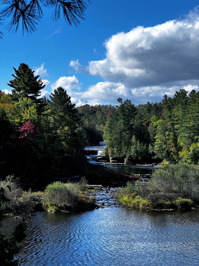 Wide view of the Tahquamenon River near the Lower Falls on a sunny day with blue sky and early fall color beginning to show in the treetops