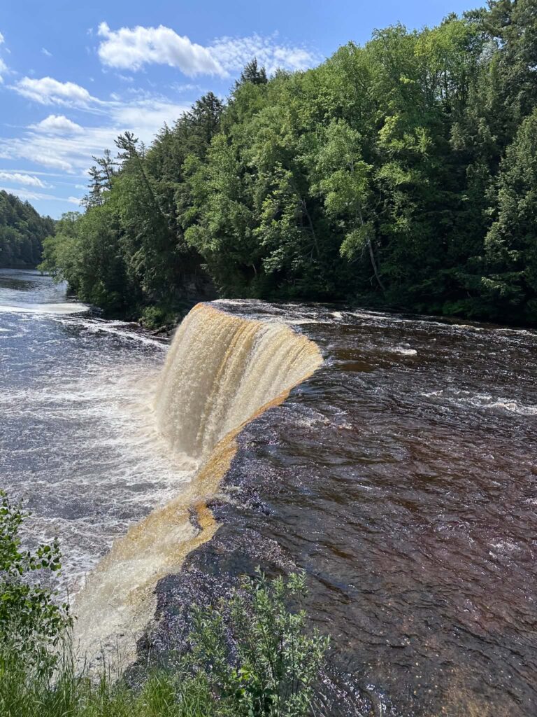 Curving view of Upper Tahquamenon Falls with amber water and wooded shoreline