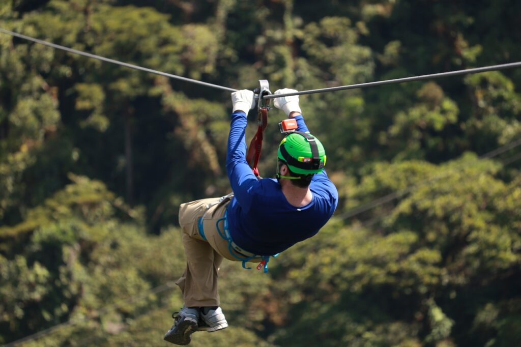 man with green helmet zip lining through the trees