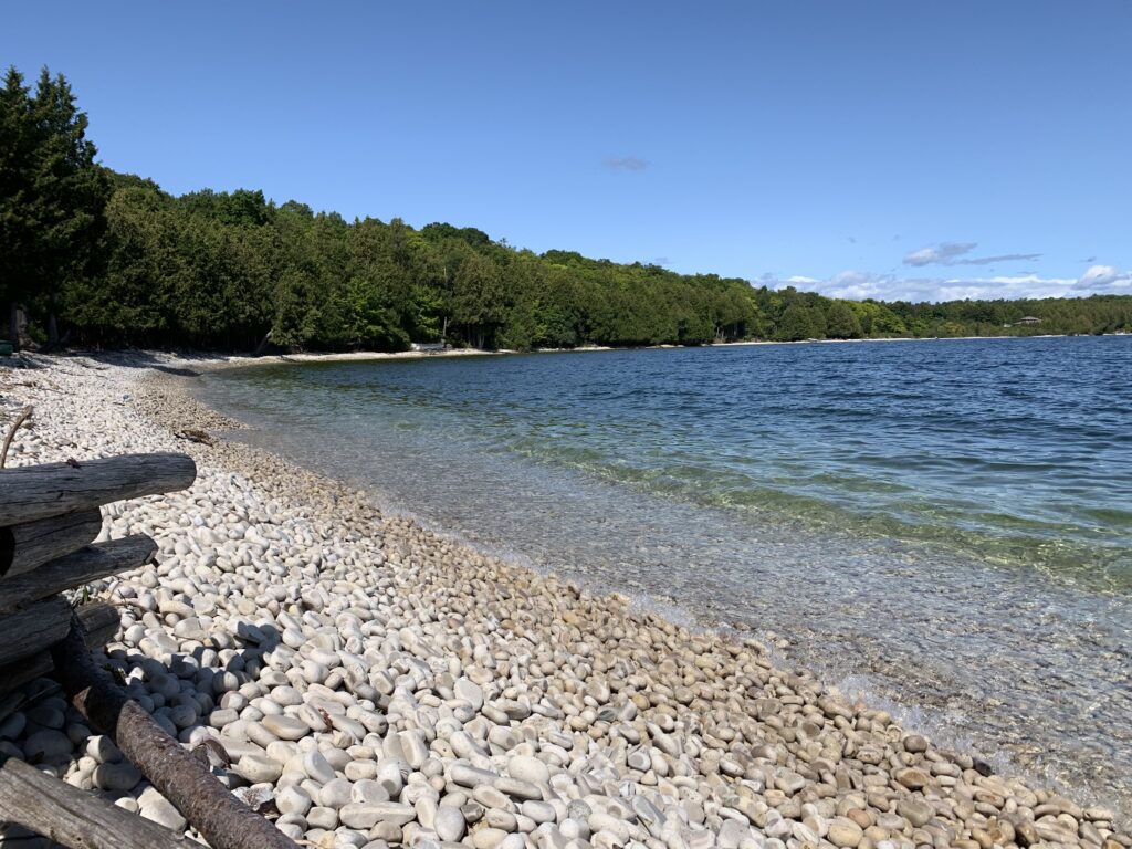 Washington Island at the tip of the Door County peninsula — a secret cove of smooth limestone pebbles, crystal clear water, and summer forest that no other Lake Michigan beach town can replicate.