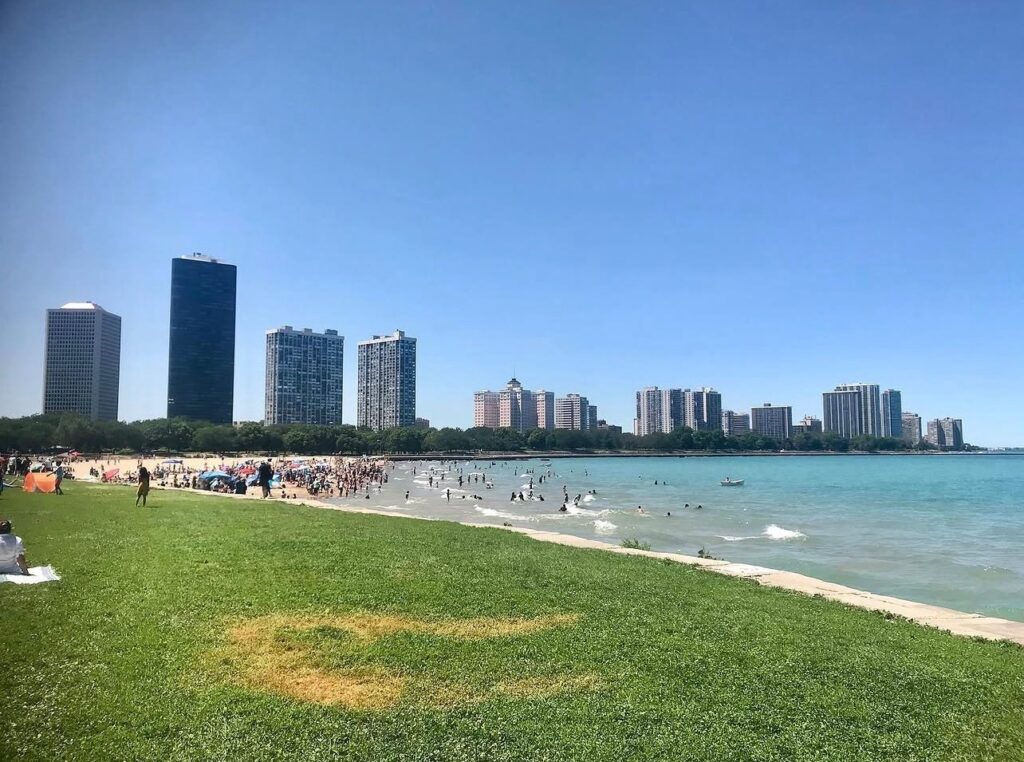 Chicago lakefront on a summer afternoon — packed beach, turquoise Lake Michigan, and the full city skyline behind. This is not a beach town. It is a beach metropolis