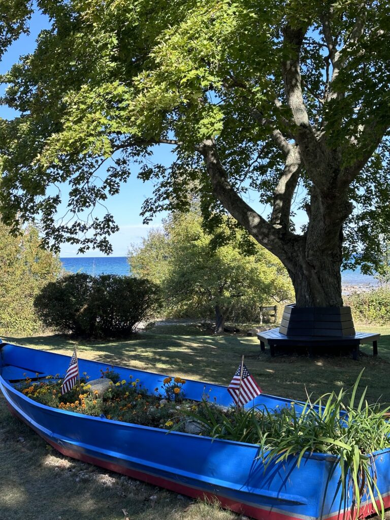 Grand Traverse Lighthouse grounds on the Leelanau Peninsula — a repurposed boat garden and summer trees frame the Lake Michigan view