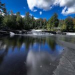 The Tahquamenon River near the Lower Falls with a dramatic storm-gray sky reflected in the calm dark water