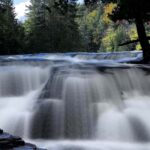 Vertical long-exposure photograph of the Lower Tahquamenon Falls with silky smooth water and a misty atmosphere rising from the cascade