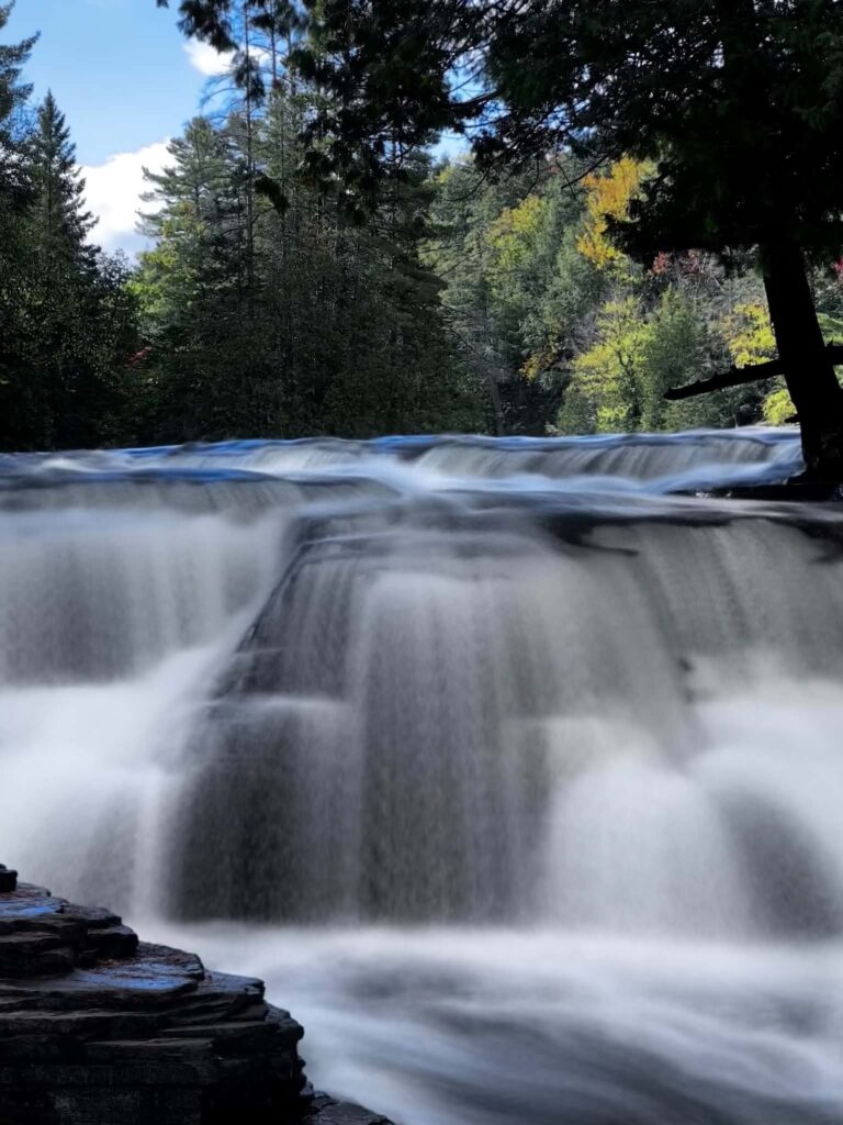 Vertical long-exposure photograph of the Lower Tahquamenon Falls with silky smooth water and a misty atmosphere rising from the cascade