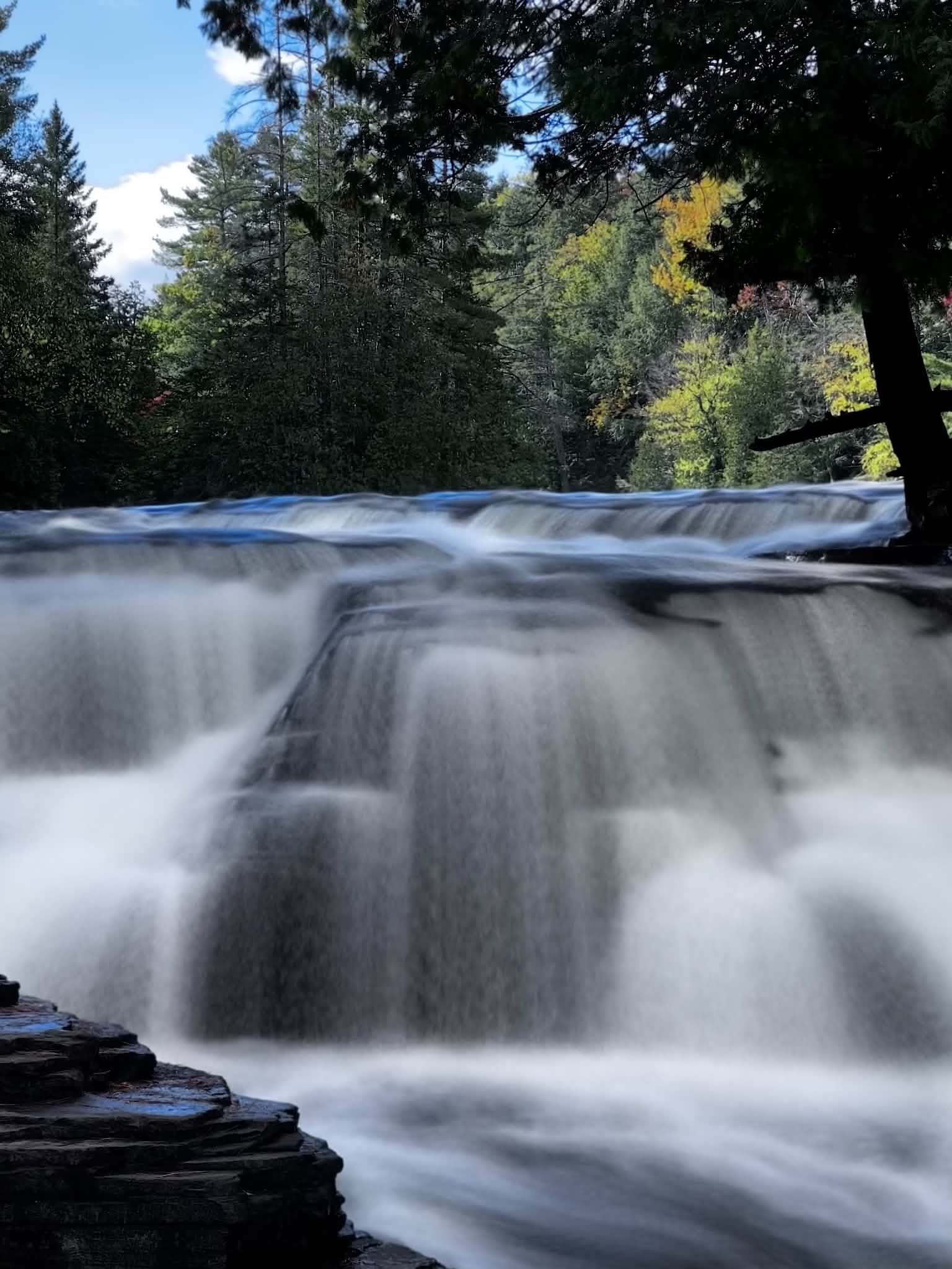 Vertical long-exposure photograph of the Lower Tahquamenon Falls with silky smooth water and a misty atmosphere rising from the cascade