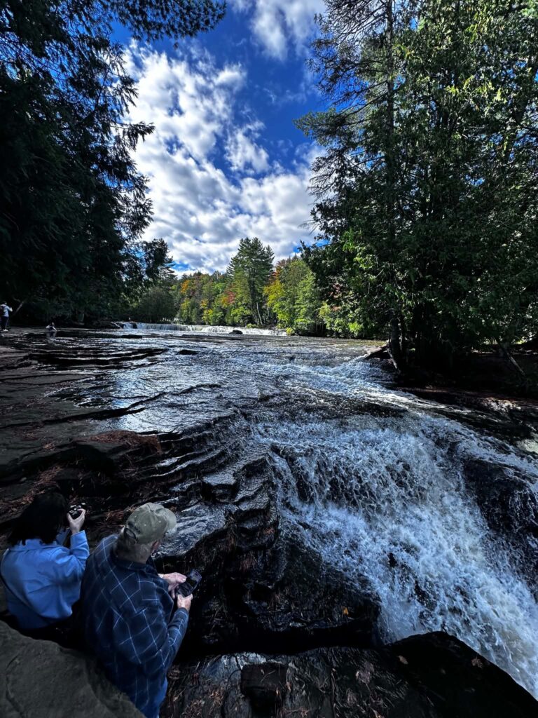 Long-exposure photograph of the Lower Tahquamenon Falls with silky smooth blurred water flowing over dark rocks under a dramatic sky
