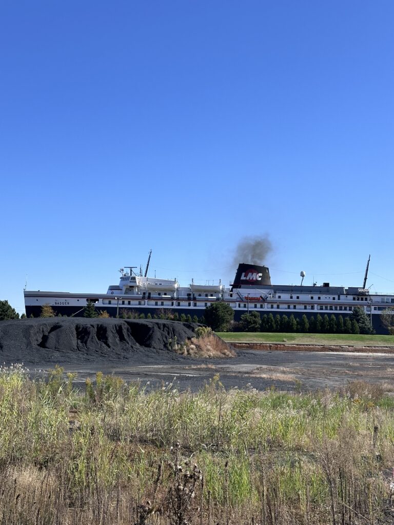 SS Badger full profile docked at Manitowoc Wisconsin with LMC smokestack coal smoke and coal pile in foreground Lake Michigan Carferry
