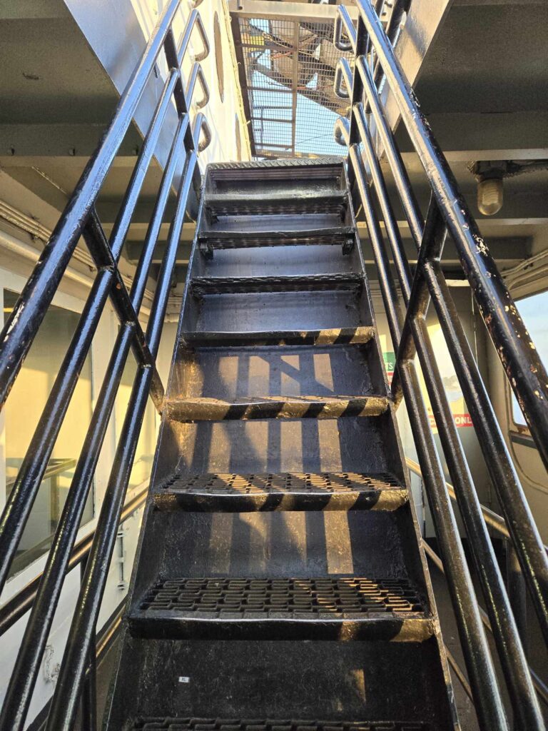 Steep interior staircase on SS Badger Lake Michigan ferry showing narrow metal steps and railings between passenger decks accessibility warning