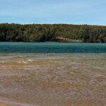 Sandy Lake Superior beach with turquoise water and wooded Pictured Rocks cliffs across the bay