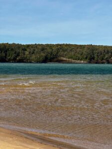 Sandy Lake Superior beach with turquoise water and wooded Pictured Rocks cliffs across the bay
