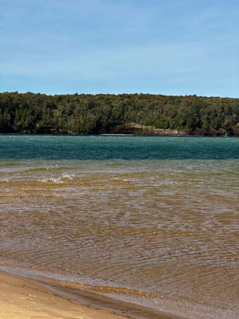 Sandy Lake Superior beach with turquoise water and wooded Pictured Rocks cliffs across the bay