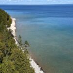 A sweeping elevated view of Mackinac Island's wooded Lake Huron shoreline, with the paved perimeter road tracing the coast