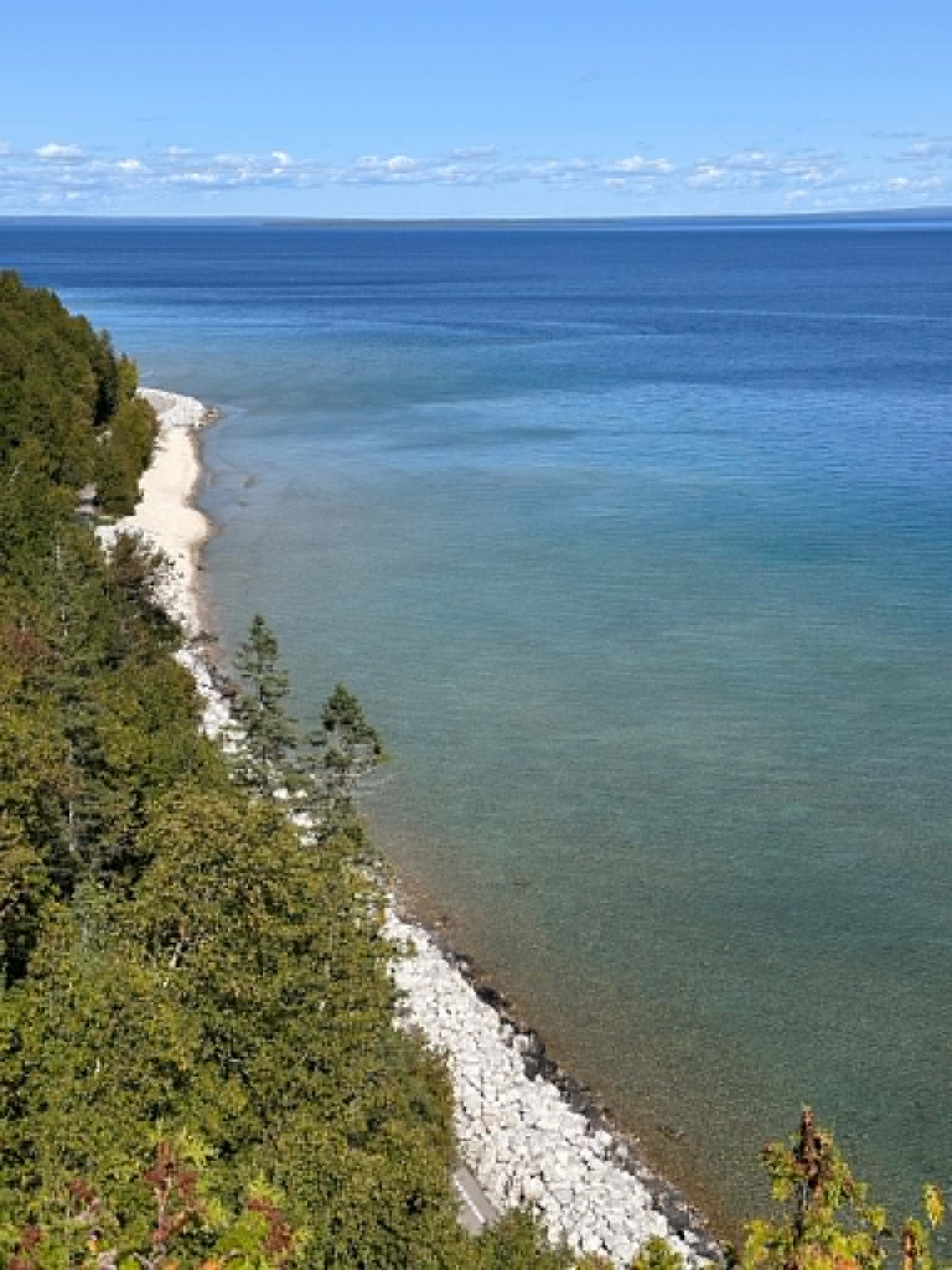 A sweeping elevated view of Mackinac Island's wooded Lake Huron shoreline, with the paved perimeter road tracing the coast