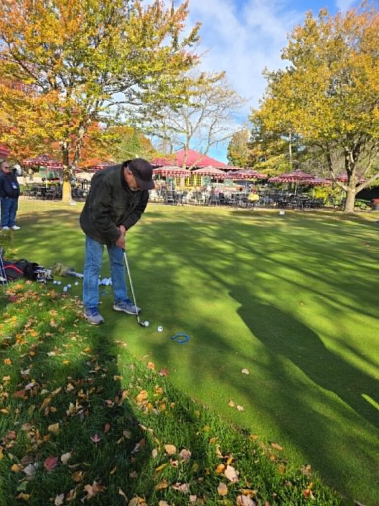 Visitor practicing miniature golf on the Grand Hotel grounds amid autumn trees and gardens on Mackinac Island.