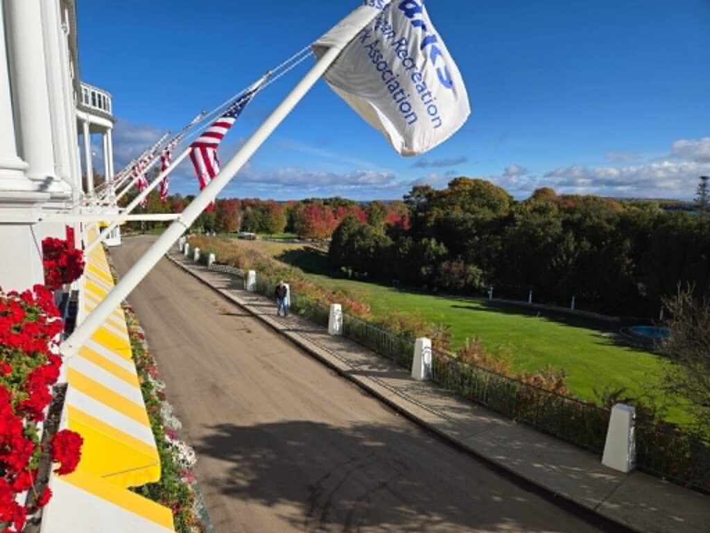 View from the Grand Hotel balcony overlooking its lawn, flower boxes, flags, and autumn-colored trees.